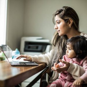 Mother Multi Tasking With Infant Daughter In Home Office