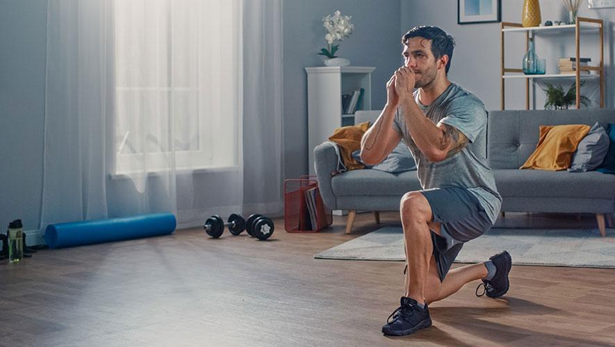 Strong Athletic Fit Man In T Shirt And Shorts Is Doing Forward Lunge Exercises At Home In His Spacious And Bright Apartment With Minimalistic Interior designer