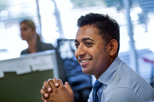 Smiling Businessman With Hands Clasped Looking Away In Office